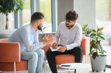 Psikolog, modern ofiste terapi seansı sırasında erkek hastaların sorunlarını dinlerken not alıyor.