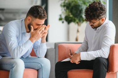 Psikolog terapi seansında erkek hastaların sorunlarını dinlerken not alıyor.