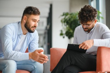 Psikolog, ofiste terapi seansı sırasında erkek hastaların sorunlarını dinlerken not alıyor.