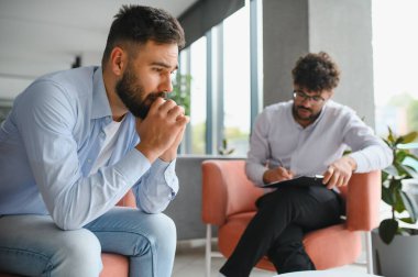 Psikolog, modern ofiste terapi seansı sırasında erkek hastaların sorunları hakkında konuşmalarını dinlerken not alıyor.