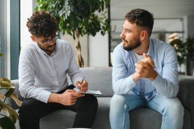 Psikolog, ofiste terapi seansı sırasında erkek hastaların sorunlarını dinlerken not alıyor.