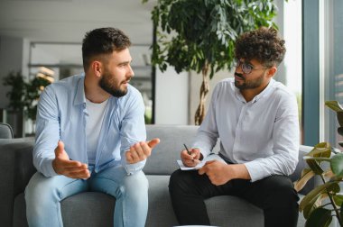 Psikolog, modern ofiste terapi seansı sırasında erkek hastaların sorunları hakkında konuşmalarını dinlerken not alıyor.