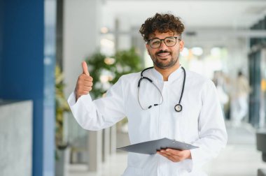 Kendine güvenen Arap doktor, sağlık hizmetlerinde olumlu ve başarılı olduğunu belirterek sağlık raporlarını tutarken iyi niyet gösteriyor.