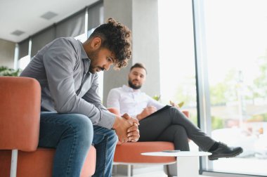 Modern bir ofiste terapi seansında not alan danışmandan psikolojik destek alan üzgün bir adam.