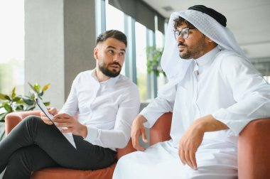 Uluslararası operasyon yöneticisi, Suudi iş ortağına bir panoda geleneksel kandura giyen bir belge gösteriyor.