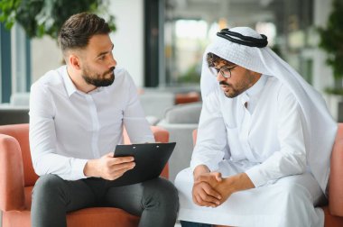 Uluslararası operasyon yöneticisi, Suudi iş ortağına geleneksel kandura giyen bir belgeyi panoda gösteriyor.