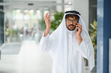 Başarılı bir girişimci akıllı bir telefonla konuşurken, parlak, modern bir ofis lobisinde, güven ve profesyonellik yayıyor.