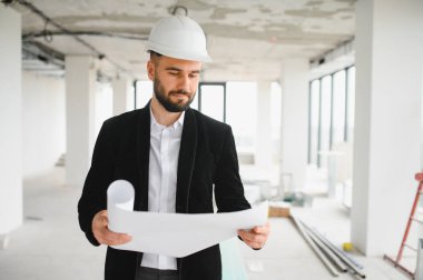 Bir inşaat sahasının planlarını inceleyen mimar, proje planlarının hassasiyet ve güvenliğe odaklanırken planlarla aynı hizaya getirilmesini sağlıyor