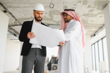 Mimar ve Arap yatırımcı, inşaat sahasında inşaat projesiyle ilgili planlarını tutuyorlar.