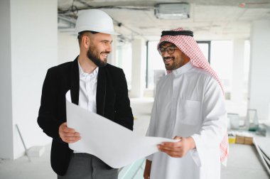 İnşaat halindeki bir binanın planlarını tartışırken gülümseyen mimar ve Arap yatırımcı, gelecekteki kalkınma planları üzerinde işbirliği yapıyor