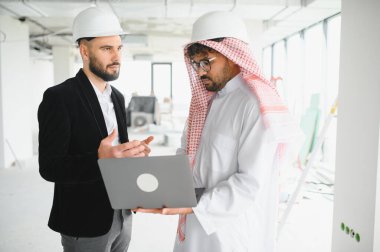 İki mimar inşaat alanındaki bir dizüstü bilgisayarın planlarını inceliyor, bina planlarını ve ilerlemeyi tartışıyorlar.