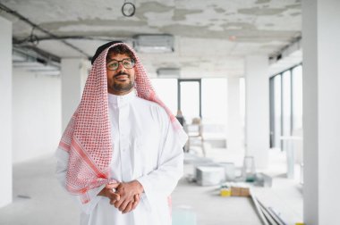 Kendine güvenen Arap işadamı inşaat halindeki bir binada duruyor ve yeni bir iş merkezine yaptığı yatırımı denetliyor.