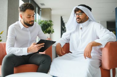 Uluslararası operasyon müdürü, Suudi iş ortağıyla yaptığı toplantıda geleneksel kandura gibi giyinmiş bir şekilde not alıyor.