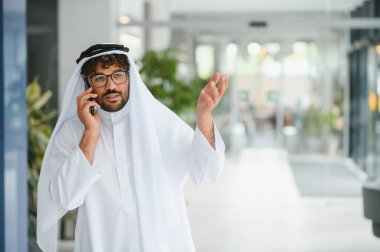 Başarılı girişimci iş konularını akıllı telefonuyla tartışır, çağdaş bir ofis alanında konuşurken el kol hareketi yapar.