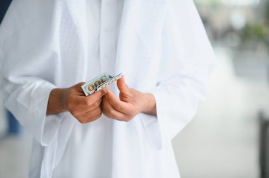 Bir Arap işadamının 100 dolarlık banknotları sayıp, kapalı alanda zenginlik ve mali yönetim sergilemesine yakından bakın.