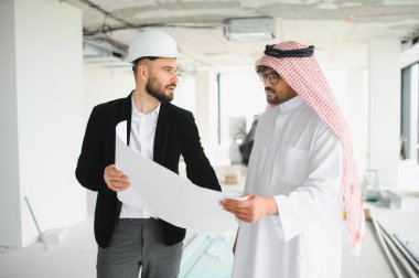 İnşaat halindeki bir binanın içinde Arap yatırımcının planlarını gösteren bir mimar.