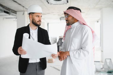 İnşaat halindeki bir binanın içinde Arap yatırımcının planlarını gösteren bir mimar.