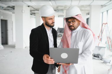Arap yatırımcı ve inşaat mühendisi tamamlanmamış binanın içinde dizüstü bilgisayar kullanarak inşaat projesini tartışıyor