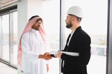 Arap işadamı ve mimar tokalaşıyor, modern bir iş merkezi için önemli bir anlaşmayı sonuçlandırıyor, başarılı işbirliğinin altını çiziyor