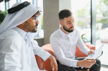 Operasyon müdürü uluslararası bir iş toplantısında Suudi iş ortağına geleneksel kandura giyen bir belge gösteriyor