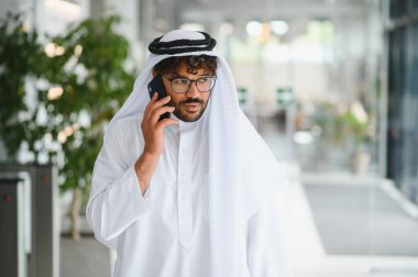 Başarılı girişimci, modern bir ofis binasında güvenle yürürken iş görüşmeleri yapıyor, profesyonellik ve hırs gösteriyor.