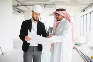 İnşaat halindeki bir binanın içinde Arap yatırımcının planlarını gösteren bir mimar.