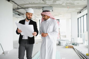 İnşaat halindeki bir binanın içinde Arap yatırımcının planlarını gösteren bir mimar.