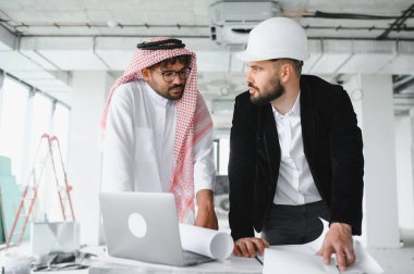 Arap yatırımcı ve mimar inşaat sahasında yapılan toplantıda planları inceleyip dizüstü bilgisayar kullanarak gayrimenkul gelişimini tartışıyorlar.