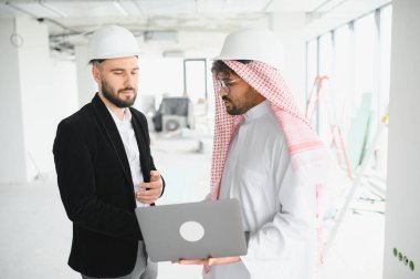 Arap yatırımcı ve inşaat mühendisi, tamamlanmamış binadaki dizüstü bilgisayarların planlarını inceliyor.