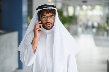 Modern ofis binasında geleneksel kandura giyen başarılı girişimci cep telefonu kullanıyor