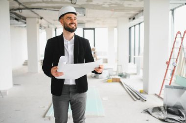 Sırıtkan mimar, inşaat alanını denetleyen ve geliştirme projesini planlayan planlar taşıyor.