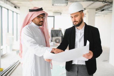 Arap işadamı ve mimar inşaat alanının planlarını inceliyor, bina planlarını ve emlak yatırımlarını tartışıyorlar