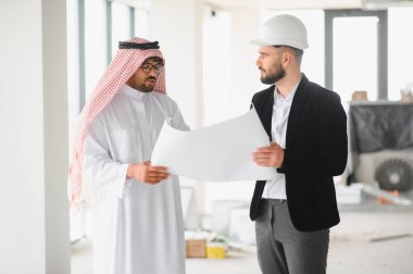 Arap yatırımcı ve mimar bir inşaat alanının planlarını inceliyor, yeni bir emlak projesinin planlarını tartışıyorlar.