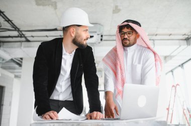 İnşaat alanında dizüstü bilgisayar kullanarak Arap yatırımcının planlarını gösteren bir mimar.