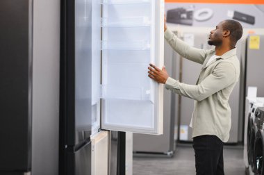 Afrika kökenli Amerikalı müşteri buzdolabının kapısını açıyor, elektronik mağazasında ya da alışveriş merkezinde yeni buzdolabı seçiyor.
