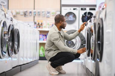Afrika kökenli Amerikalı bir adam elektronik eşya mağazasının yeni çamaşır makinesini seçiyor.