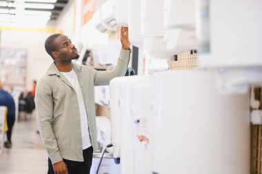 Alet dükkanında yeni klima seçen genç adam, özellikleri inceleyerek ve modelleri karşılaştırarak