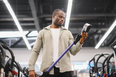 Konsantre olmuş Afro-Amerikan adam kablosuz elektrik süpürgesini seçiyor, kutunun özelliklerini okuyor.