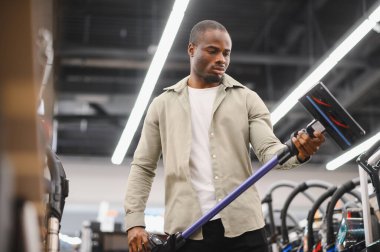 Elektrik süpürgesini kontrol eden adam, satın alma kararı vermeden önce seçenekleri değerlendiriyor ve özellikleri değerlendiriyor.