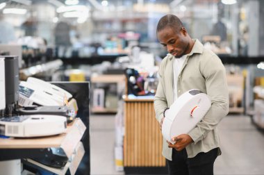 Elektronik mağazasında alışveriş yaparken elinde robot süpürge tutan bir adam satın almadan önce ürünü inceliyor.