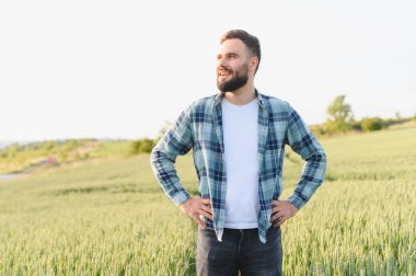 Genç tarımcı, altın buğday tarlasında güven içinde duruyor. Elleri kalçasında. Uzağa bakarken ışıl ışıl gülümsüyor.