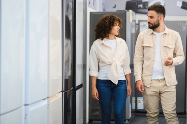 Çift elektronik mağazasını keşfediyor, ev aletlerini tartışıyor ve seçiyor. Bilgilendirilme kararı almaya odaklanmış görünüyorlar.