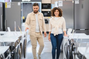 Canlı bir elektronik mağazasından ev aletleri alırken yeni bir çamaşır makinesi arayan mutlu çift.