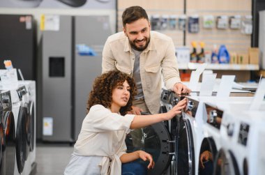 Ev aletleri mağazasından yeni çamaşır makinesi seçen mutlu çift, ev eşyaları için birlikte karar veriyorlar.