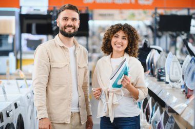 Ev aletleri mağazasında yeni bir ütü seçerken gülümseyen mutlu çift, ev eşyaları alışverişinin tadını çıkarıyor.