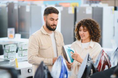 Ev aletleri mağazasında buhar ütüsü seçen genç çift, ev eşyaları alışverişi yapıyor.