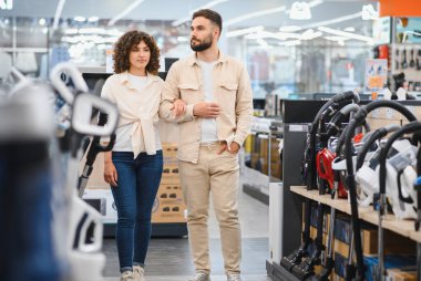 Genç çift ev aletleri dükkanına göz gezdiriyorlar. Birlikte alışveriş yaparken yeni bir elektrikli süpürge seçiyorlar.