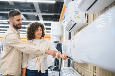 Bir elektronik mağazasında ev aletlerini seçerken klimayı işaret eden mutlu çift, birlikte alışveriş deneyimlerinin tadını çıkarıyorlar.