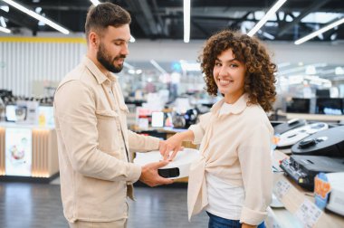 Kadın ve erkek elektronik mağazasında ev aletlerini inceliyor, seçenekleri tartışıyor ve satın alma kararlarını birlikte veriyorlar.