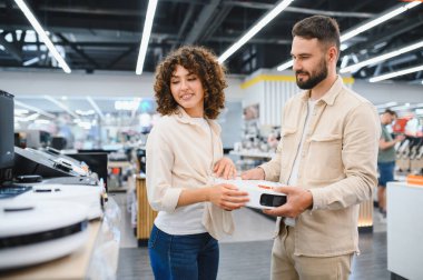 Robot elektrikli süpürge tutan genç bir çift elektronik mağazasından ev aletleri alıyor.